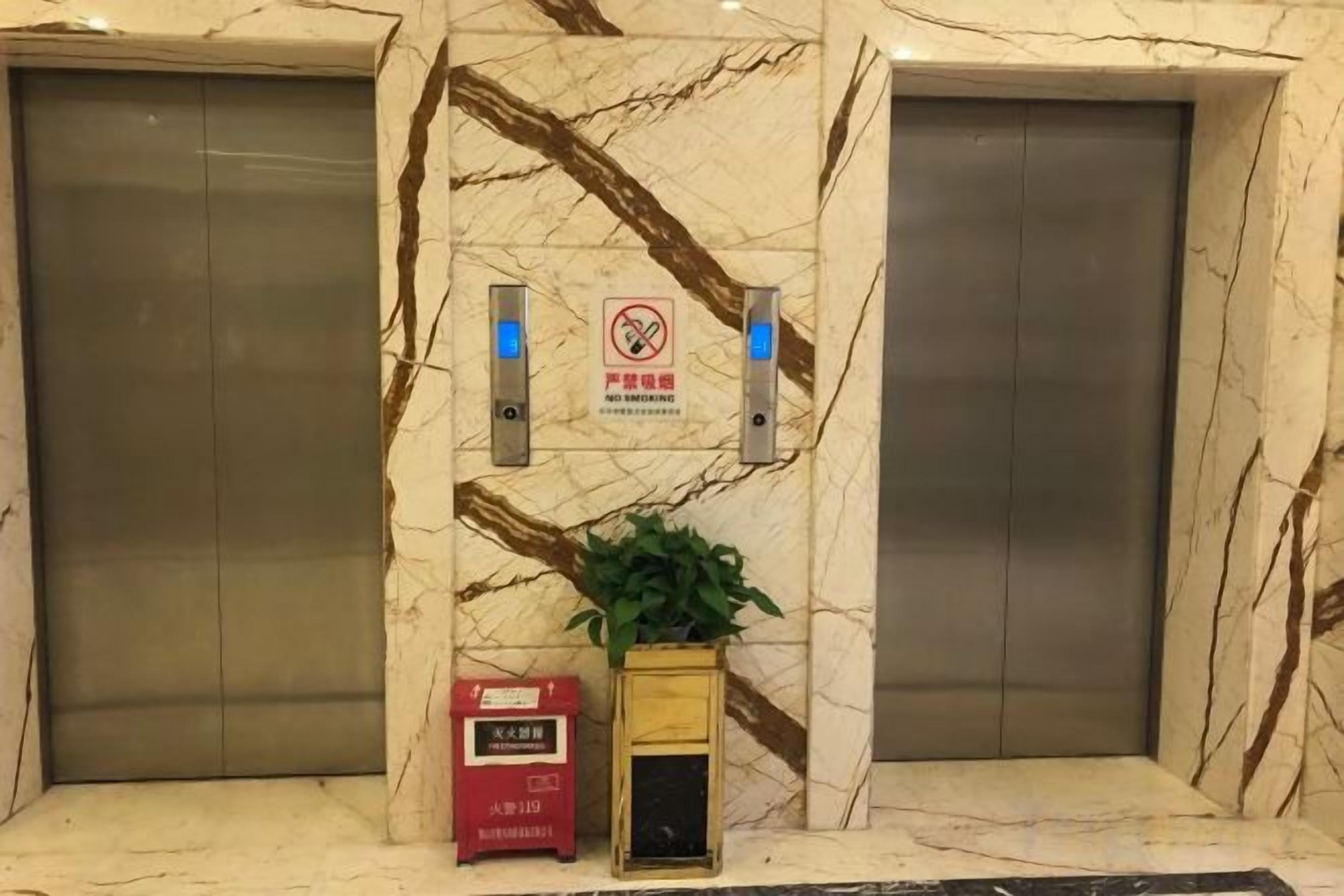 An elevator area with marble walls, two elevators, a no-smoking sign, and a fire alarm box.