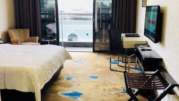 A hotel room with a large bed, a desk with a chair, a television, and a view through a glass door.