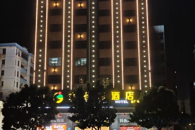 A hotel with a vertical light strip design, a prominent sign, and a tree-lined entrance.