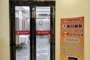 Entrada de hotel con puerta de cristal y cartel anunciando desayuno autoservicio gratuito.