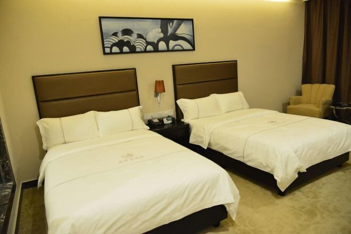 A hotel room with two beds, a nightstand, a lamp, and a chair.