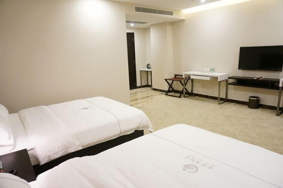 A hotel room with two beds, a desk, a chair, a television, and a small table.