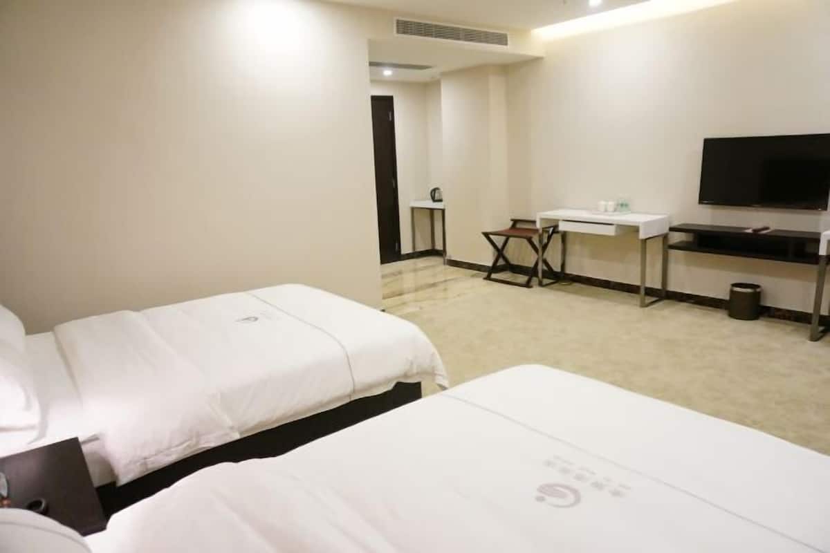 A hotel room with two beds, a desk, a chair, a television, and a small table.