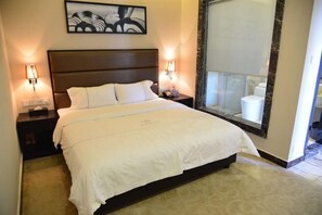 A hotel room with a large bed, two bedside lamps, a nightstand, a framed artwork above the bed, and a large mirror. - Jinbiwan Hostel (Kaiping)