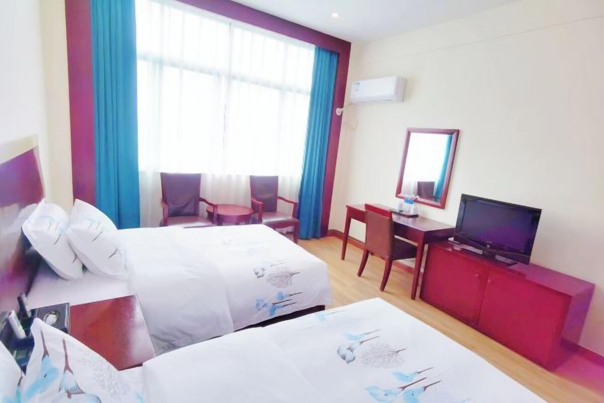 A hotel room with two beds, a desk, a television, and a red cabinet.
