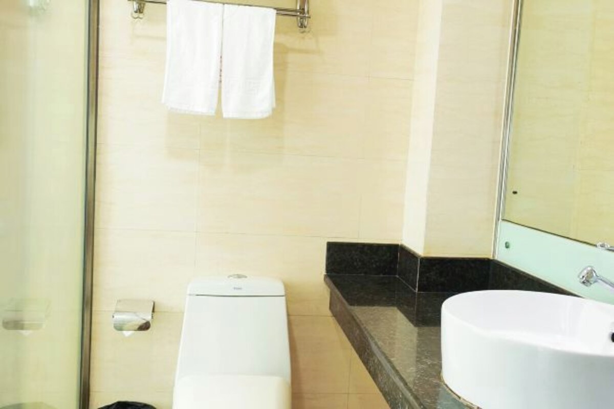 Un baño con cabina de ducha de vidrio, inodoro blanco, lavamanos con encimera negra y espejo.