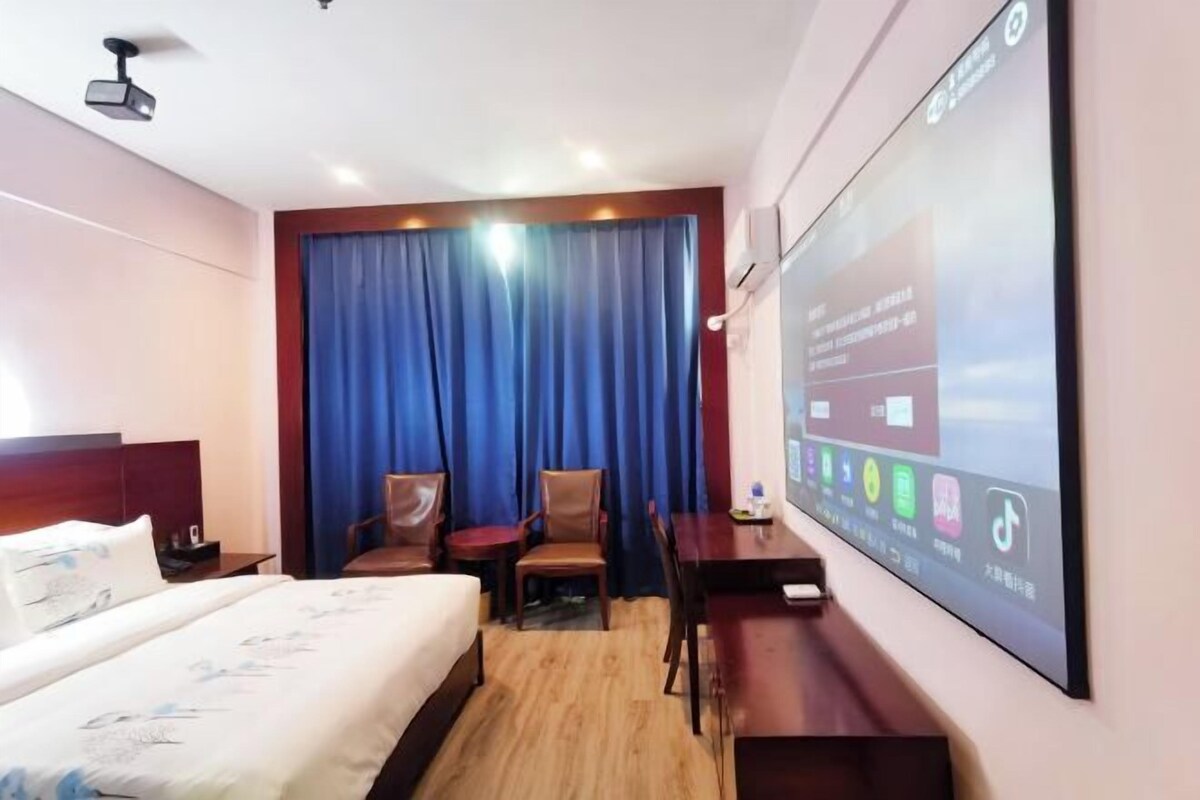 A hotel room with a bed, a desk, a chair, a TV screen, and a curtain.
