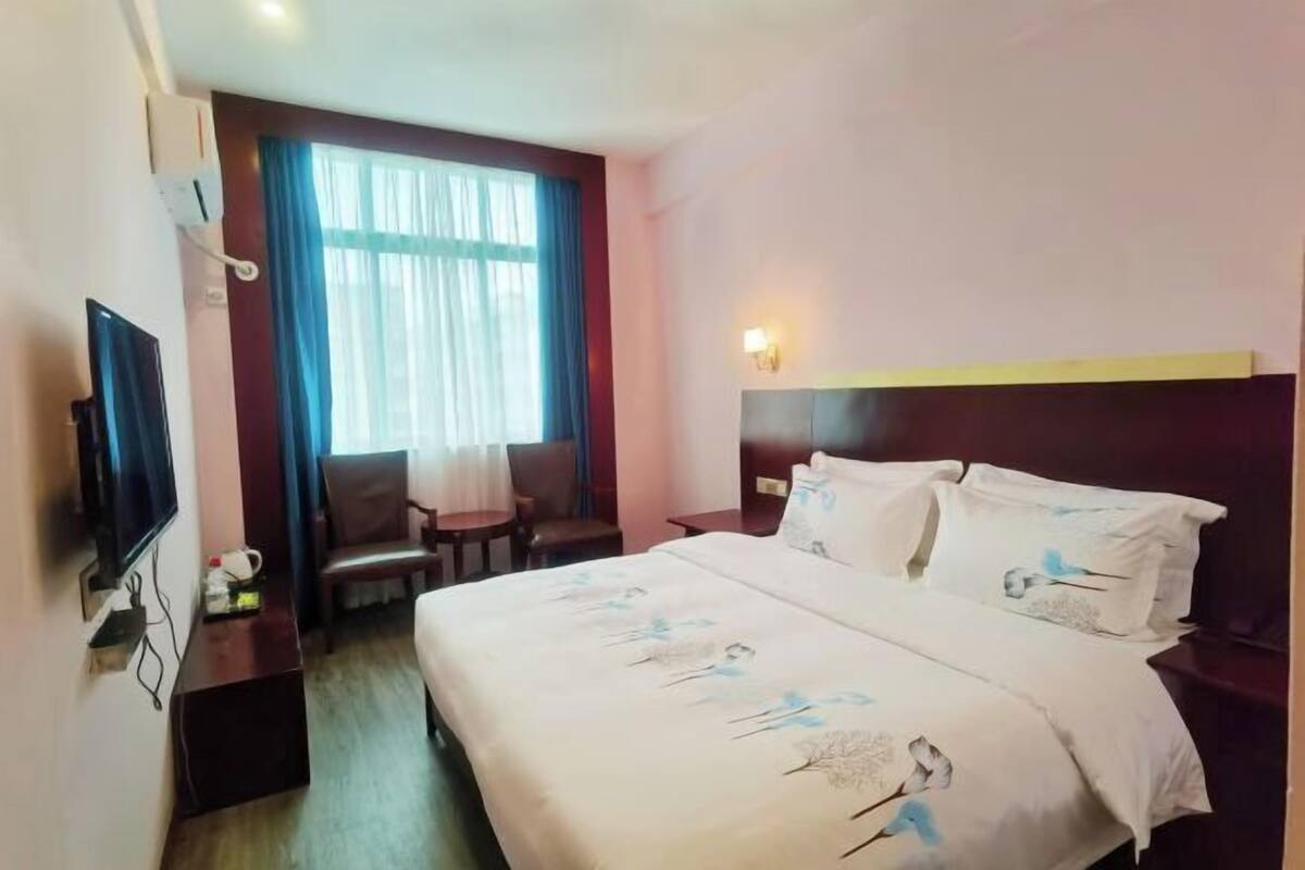 Een hotelkamer met een bed, televisie, bureau, stoel en een raam met gordijnen.