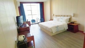 Hotellihuone, jossa on sänky, työpöytä, jossa on televisio, tuoli ja ikkuna, jossa on verhot.