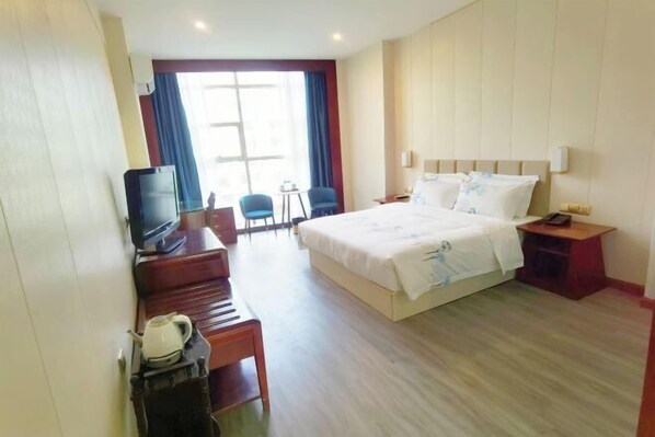 A hotel room with a bed, a desk with a television, a chair, and a window with curtains. - Deyuan Hotel (Shaoguan Nanhua Temple) (Shaoguan)