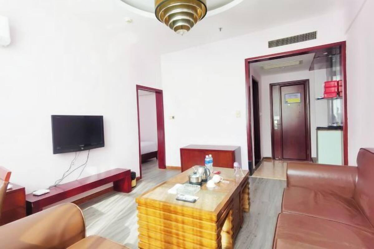 Hotelkamer met een flatscreen televisie, een houten bijzettafeltje, een rode bank en een bruine leren bank.
