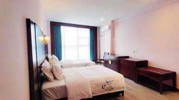 Habitación de hotel con dos camas, un escritorio, una silla, un banco y un ventanal con cortinas.