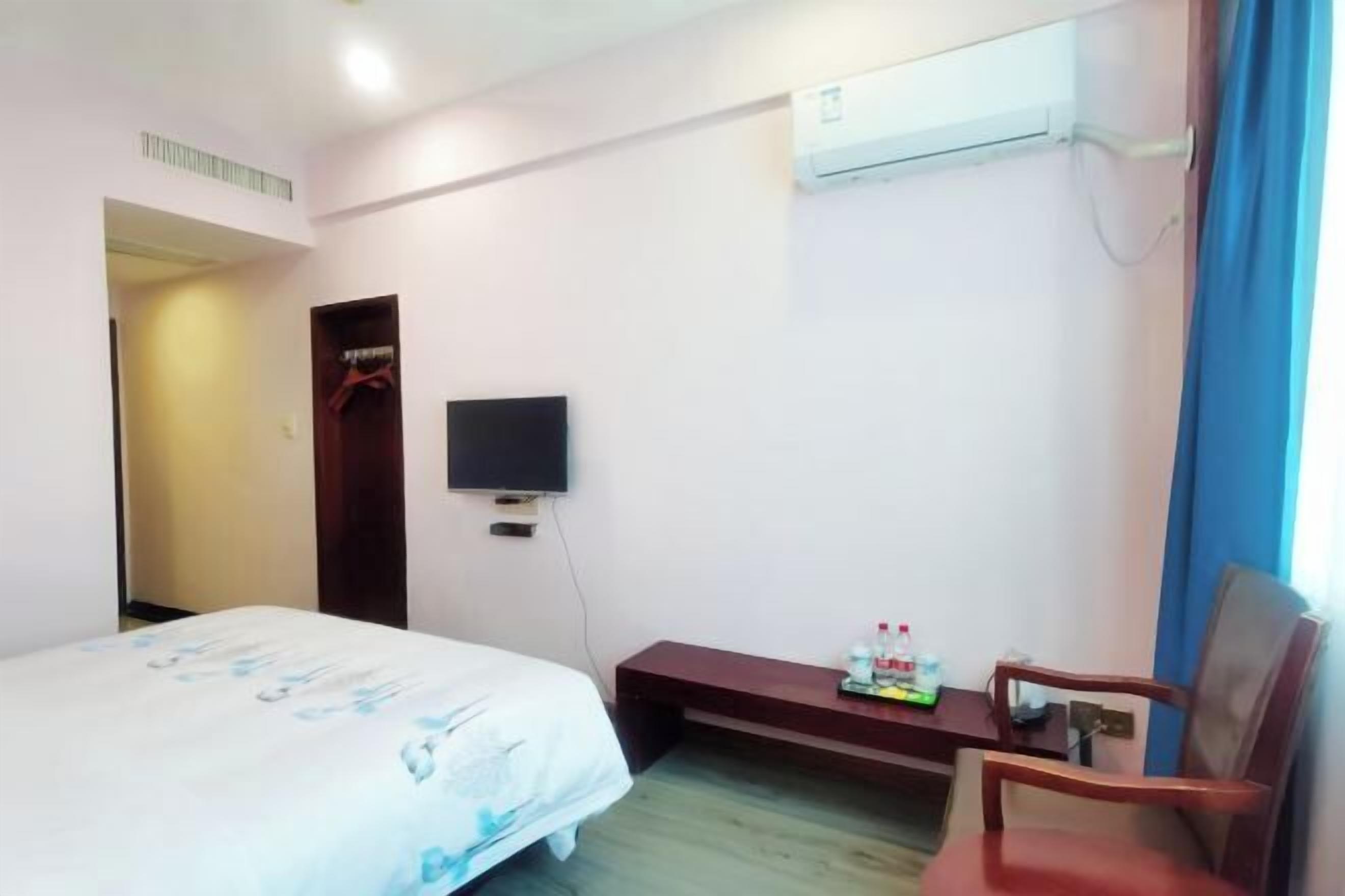 Een hotelkamer met een bed, een televisie, een bureau met een stoel en een airconditioning.