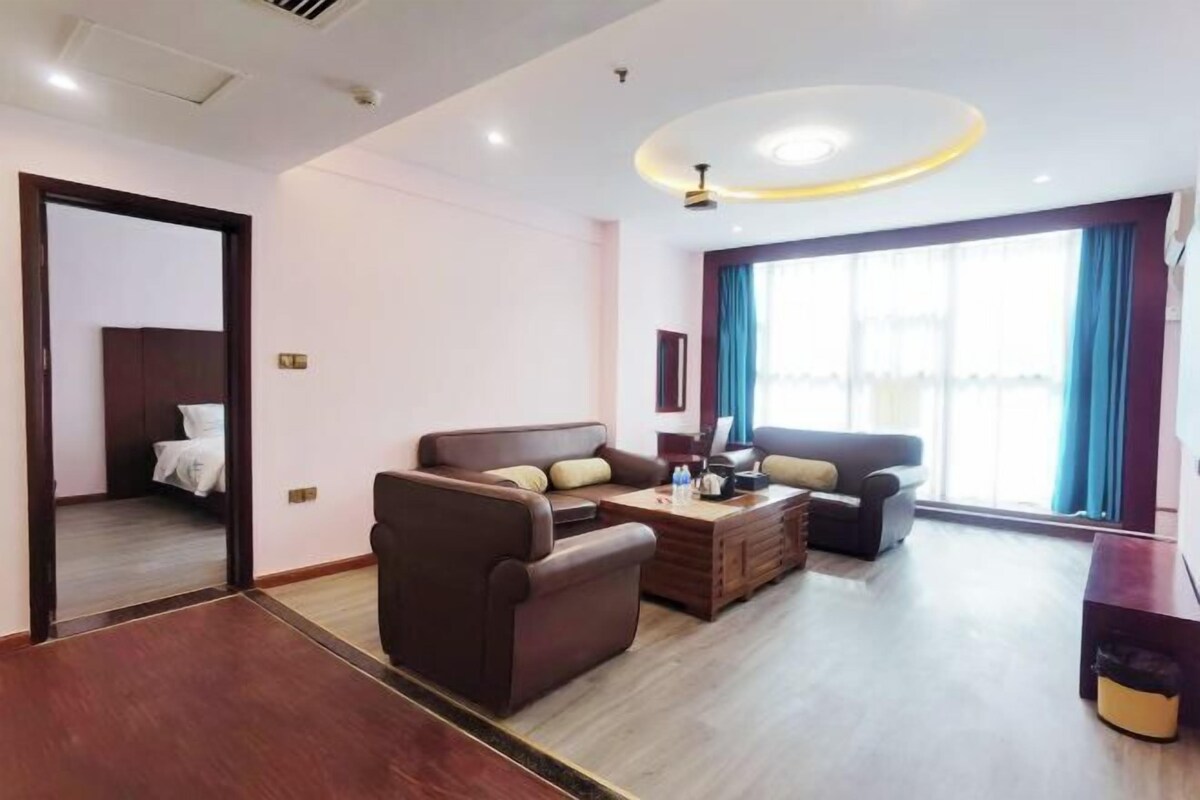 A hotel room with a bed, two sofas, a coffee table, and a large window with curtains.