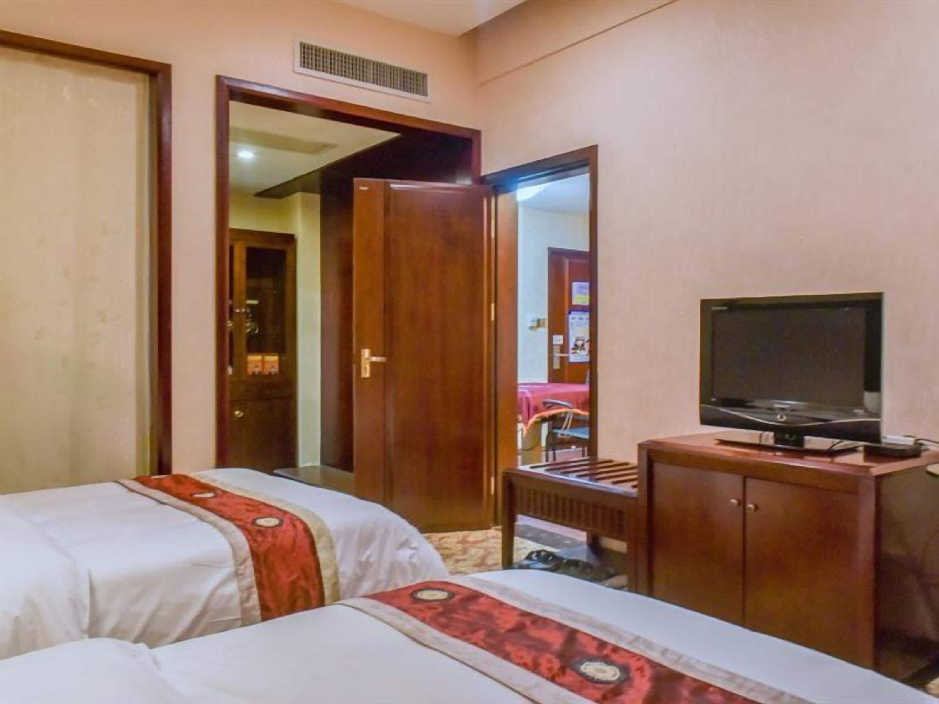 Una habitación de hotel con dos camas, un armario de madera, un televisor y un espejo.