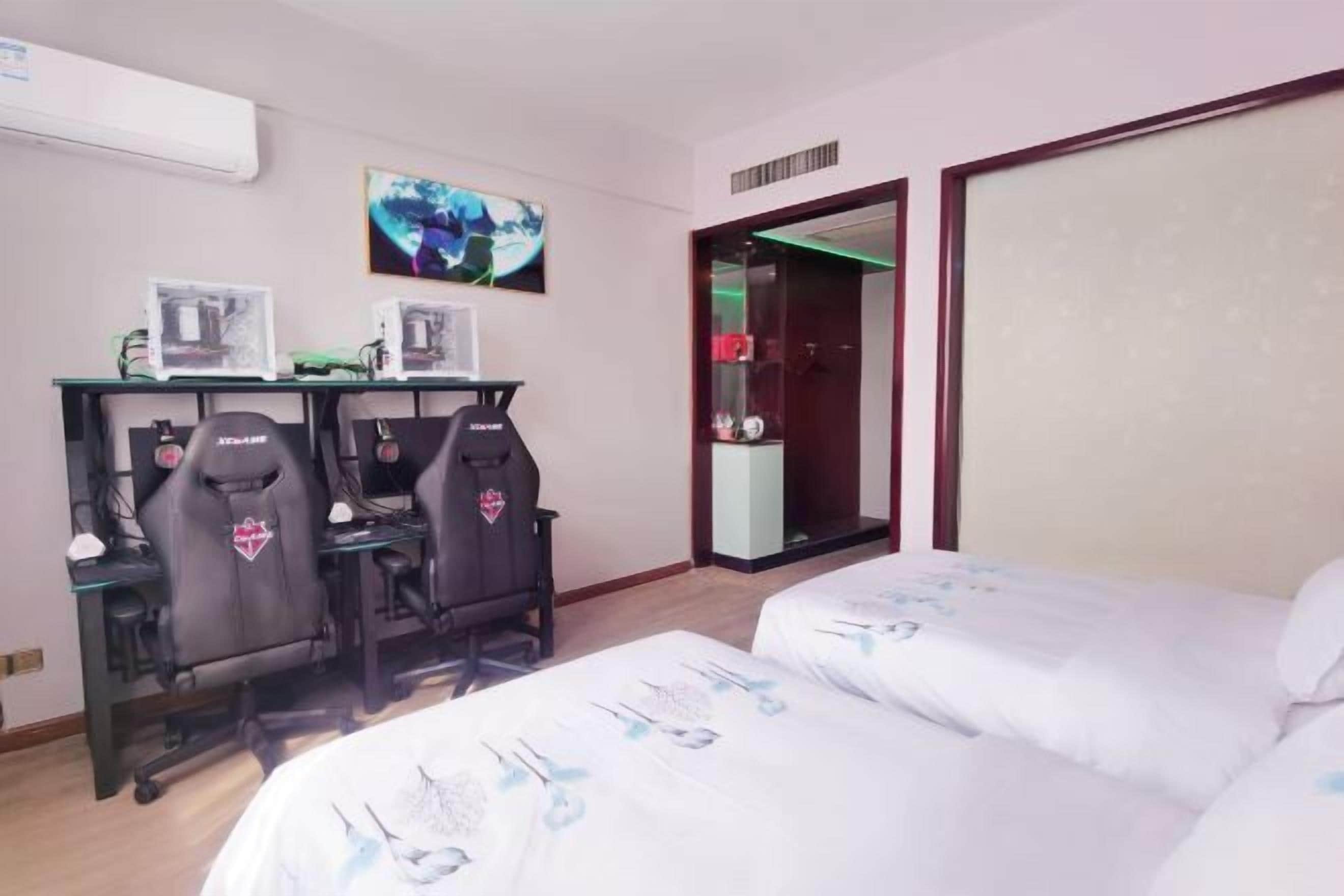 A hotel room with two beds, a desk with two gaming chairs, a TV, and a mirror.