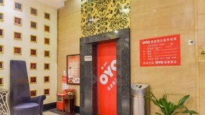 A hotel lobby with a red reception desk, a blue chair, a trash bin, and a wall with a patterned design.