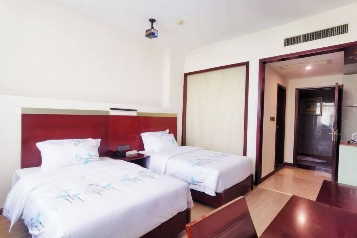 Een hotelkamer met twee bedden, een houten bureau, een rode kaptondeur en een deur naar een badkamer.