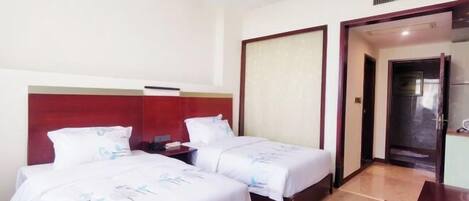 A hotel room with two beds, a wooden desk, a red headboard, and a door leading to a bathroom.