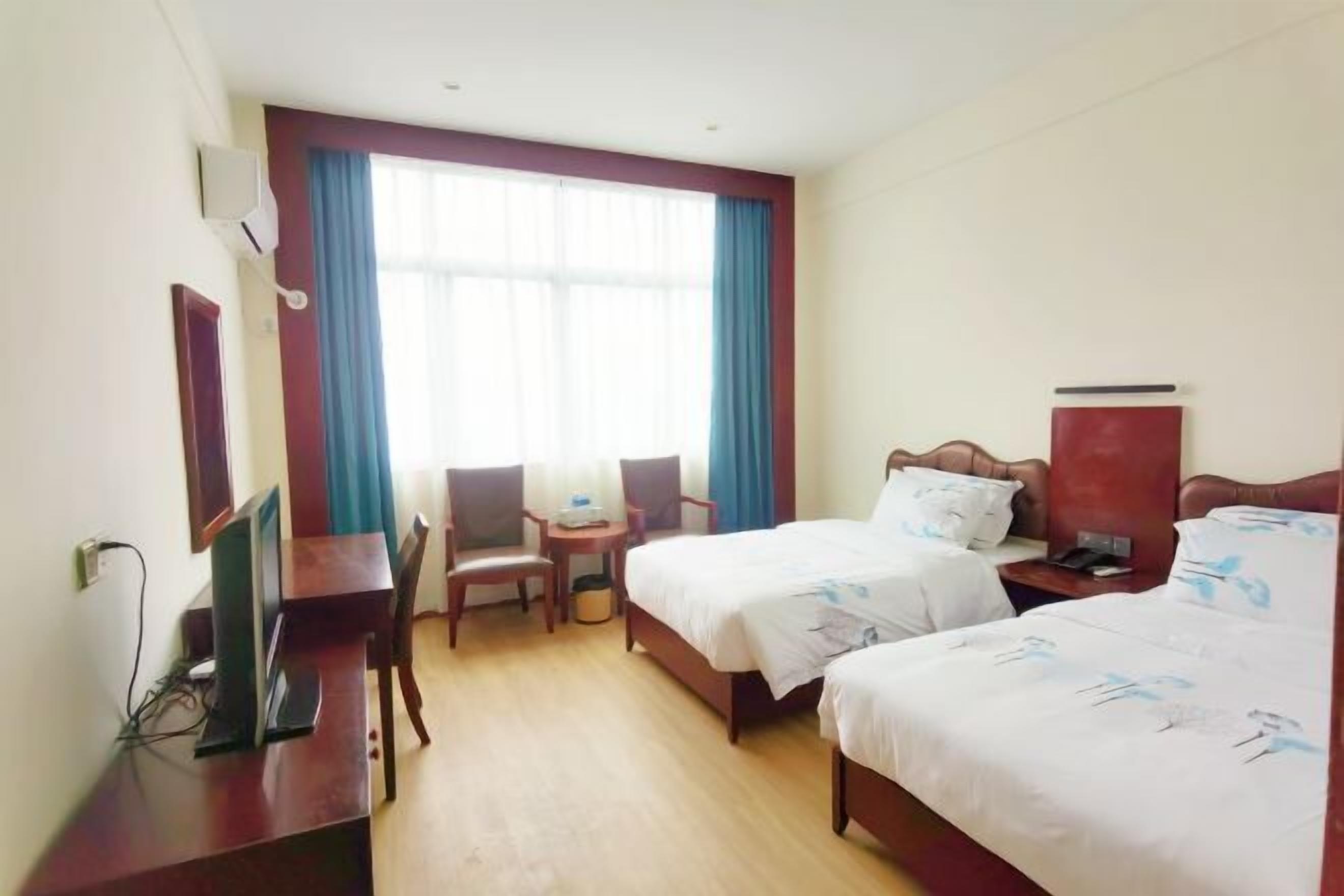 Een hotelkamer met twee bedden, een bureau, een stoel, een televisie en een raam met gordijnen.