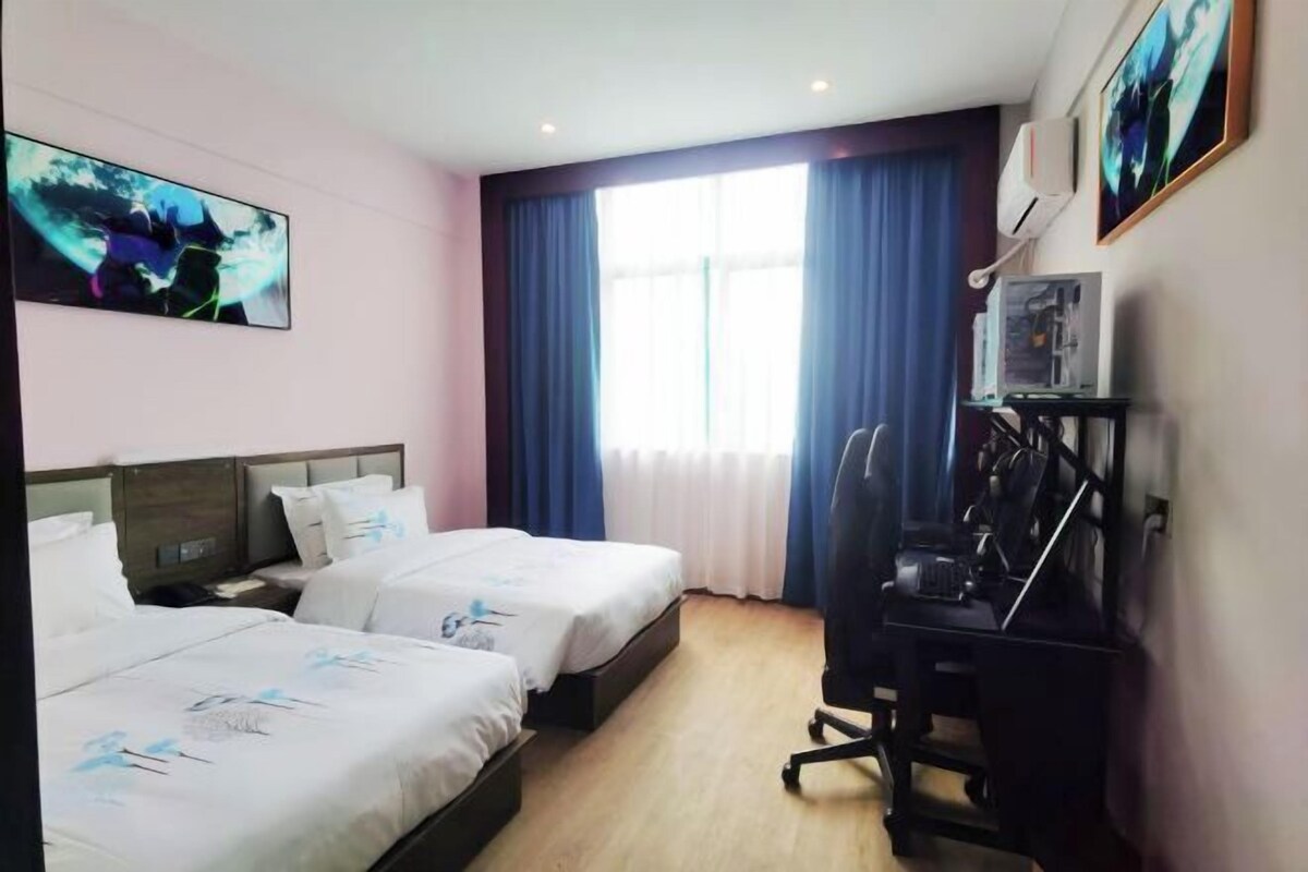 Habitación de hotel con dos camas, un escritorio, una silla, un televisor y una ventana con cortinas.