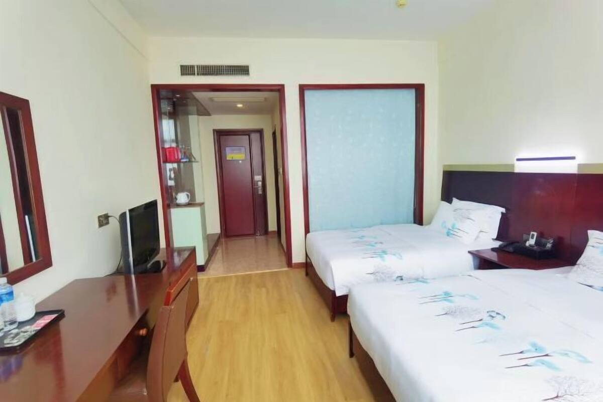 Een hotelkamer met een houten bureau, twee bedden, een televisie en een badkamers deur.