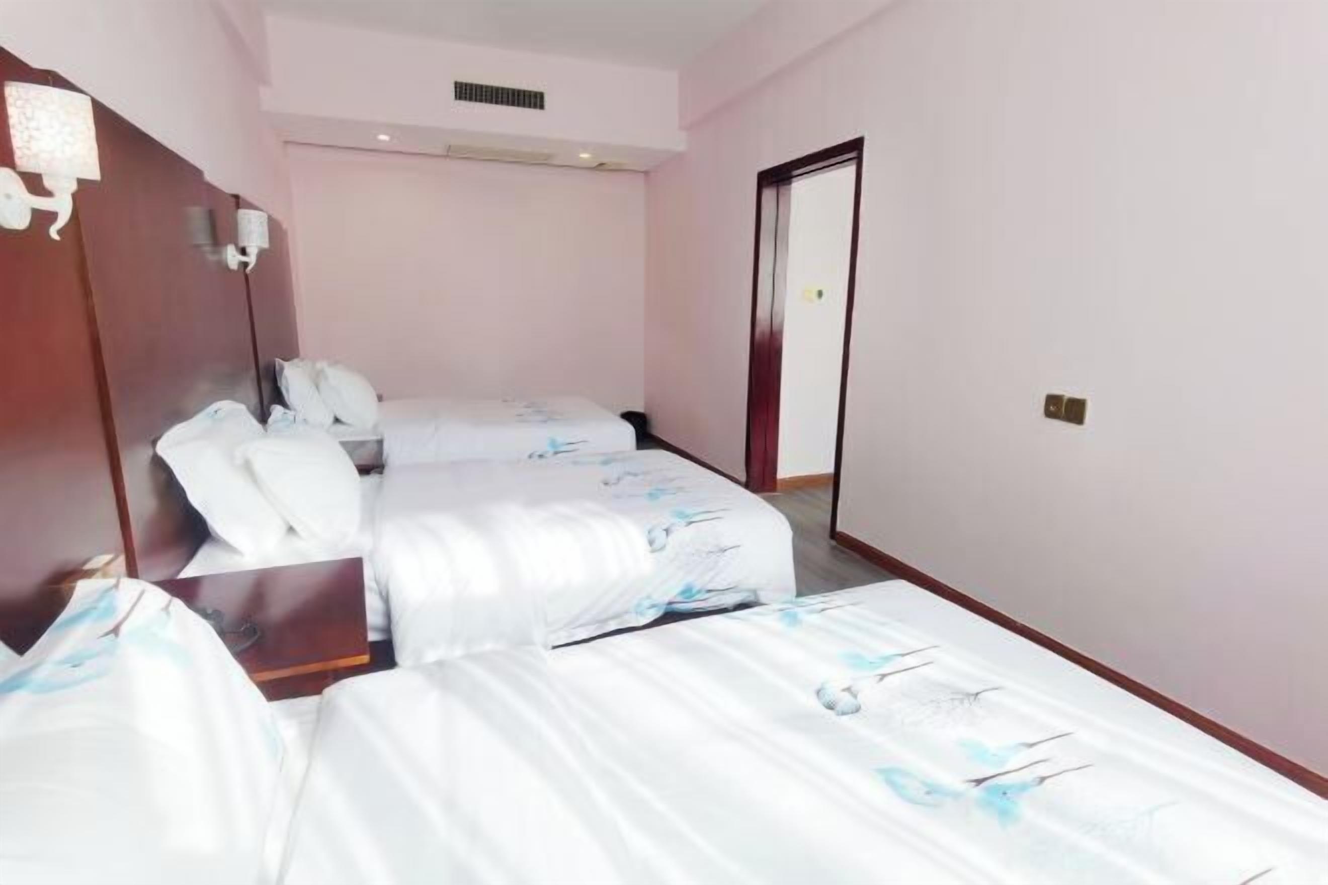 A hotel room with two beds, a wooden headboard, a bedside table, and a door.