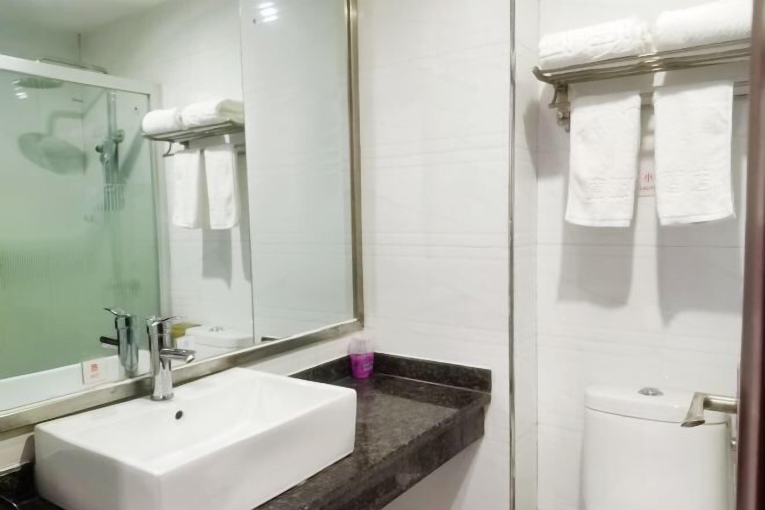 Un baño con lavamanos blanco, espejo, cabina de ducha con paredes de vidrio y toallero con toallas blancas.