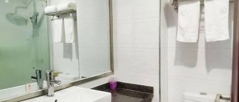 Un baño con lavamanos blanco, espejo, cabina de ducha con paredes de vidrio y toallero con toallas blancas.