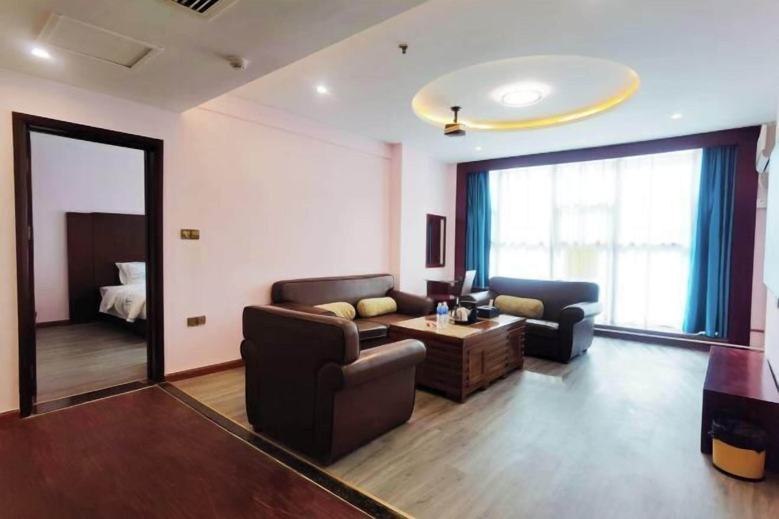 A modern living room with a sofa set, a coffee table, and a TV. There is a door leading to a bedroom.