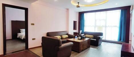 A modern living room with a sofa set, a coffee table, and a TV. There is a door leading to a bedroom.