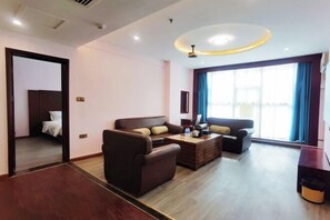 A modern living room with a sofa set, a coffee table, and a TV. There is a door leading to a bedroom.