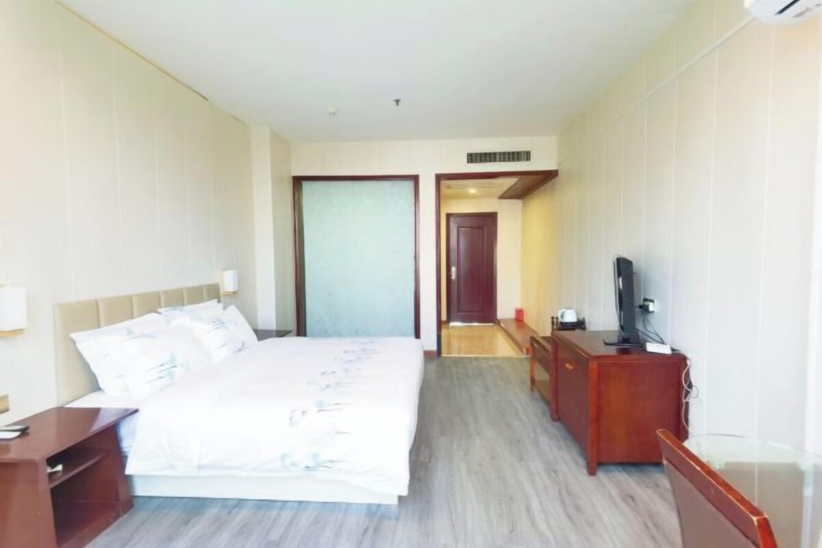 Una habitación de hotel con una cama, un escritorio, un televisor y una puerta que da a otra habitación.