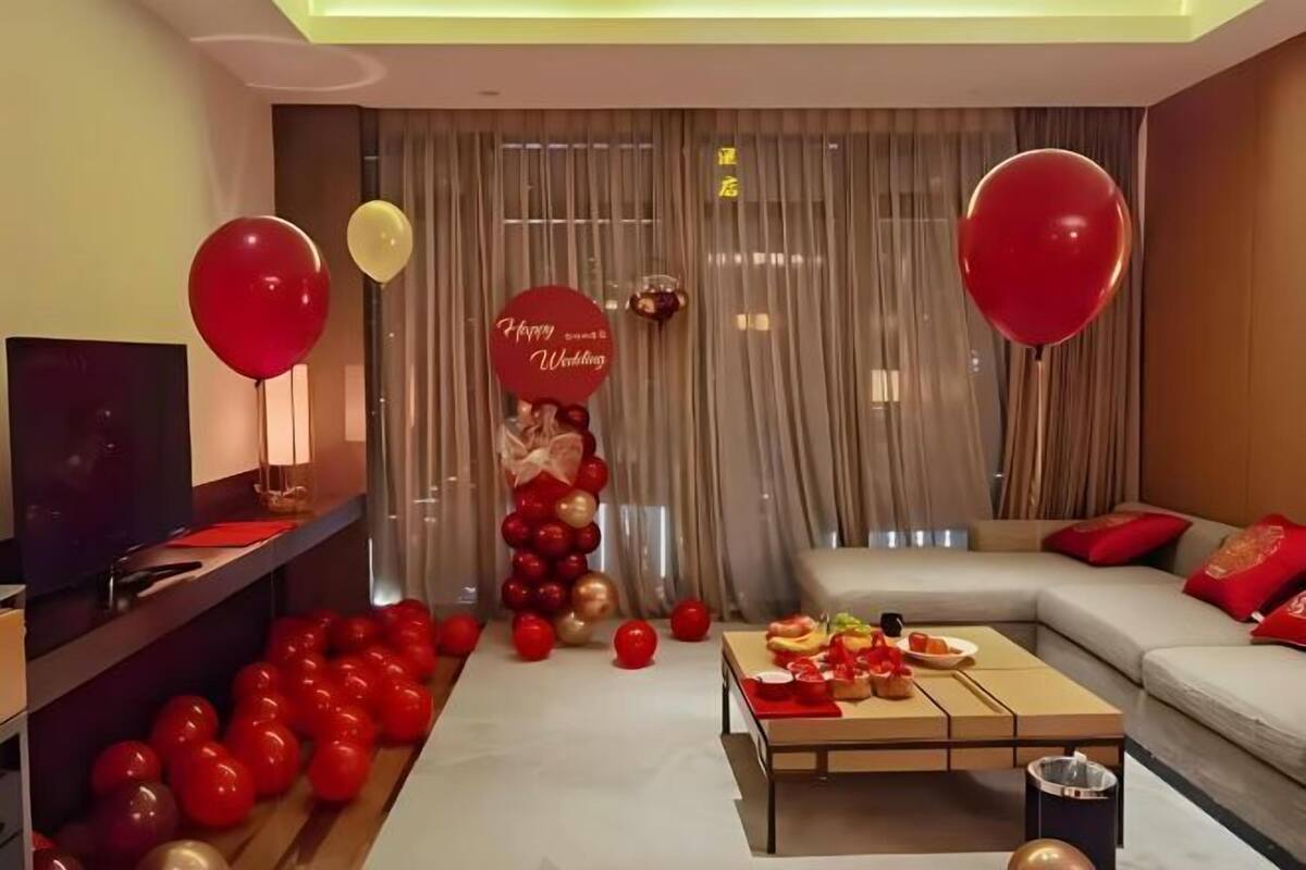 Een moderne woonkamer met een bank, een salontafel en een televisie. Er zijn ballonnen en een bord met de tekst 'Happy Wedding'.