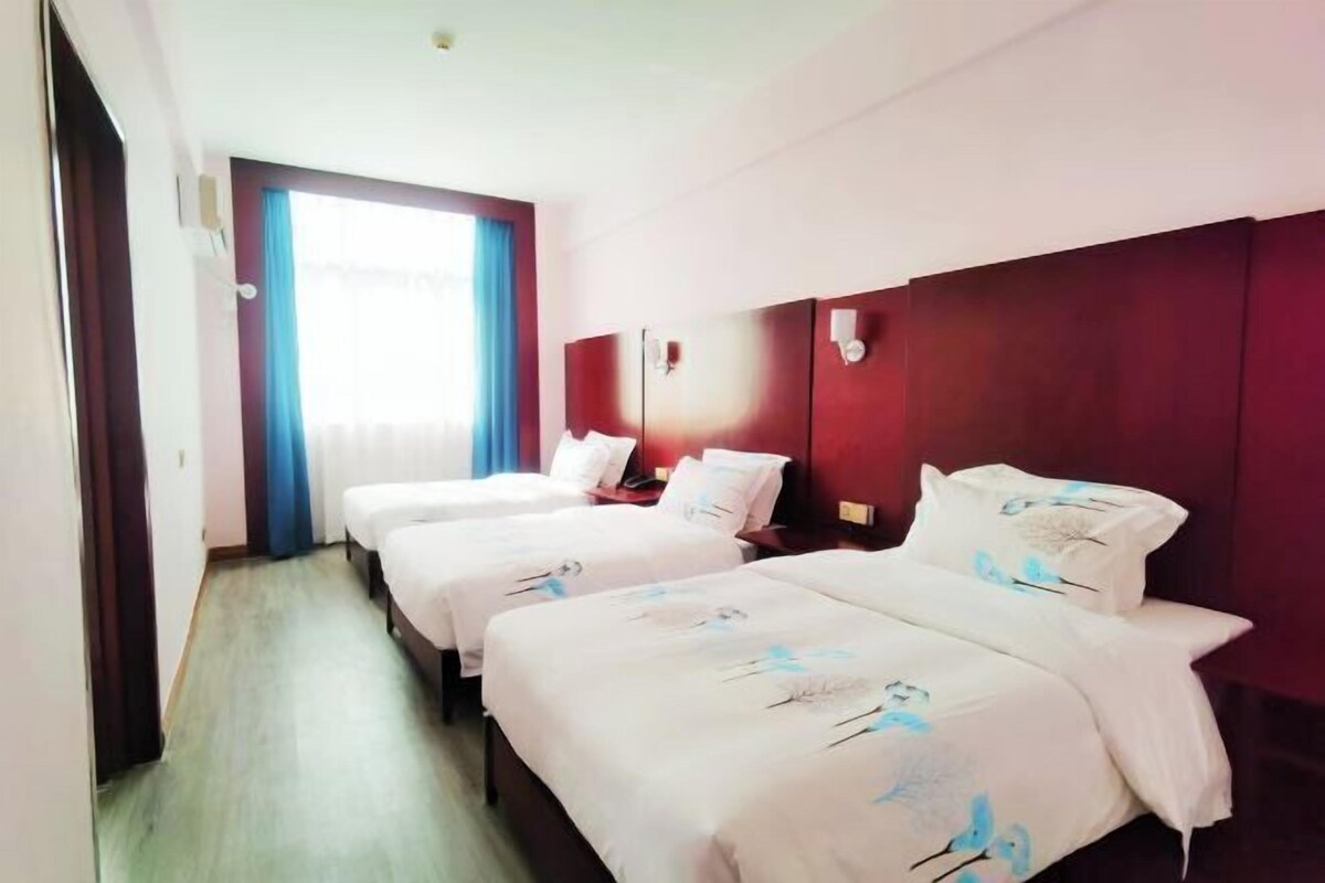 A hotel room with two beds, a large window with curtains, and a wooden floor.