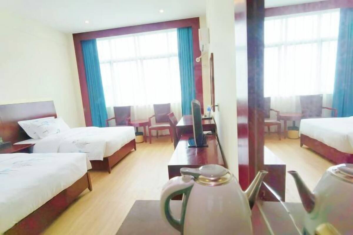 Een hotelkamer met twee bedden, een bureau, een stoel, een waterkoker en een groot raam met gordijnen.
