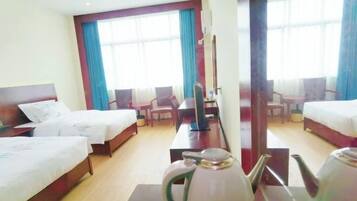 Une chambre d’hôtel avec deux lits, un bureau, une chaise, une bouilloire et une grande fenêtre avec des rideaux.
