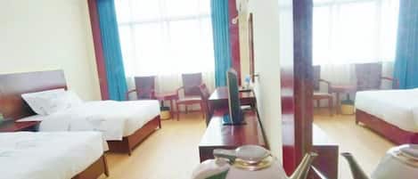 Habitación de hotel con dos camas, un escritorio, una silla, una tetera y un ventanal grande con cortinas.