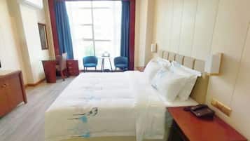 A hotel room with a bed, a desk, two chairs, a small table, and a window with curtains.