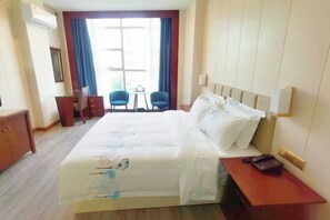 A hotel room with a bed, a desk, two chairs, a small table, and a window with curtains. - Deyuan Hotel (Shaoguan Nanhua Temple) (Shaoguan)