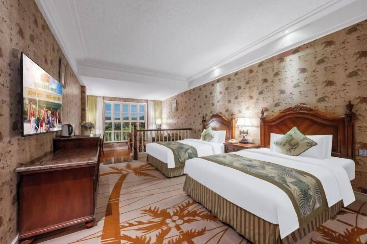 A hotel room with two beds, a desk, a television, and a window.