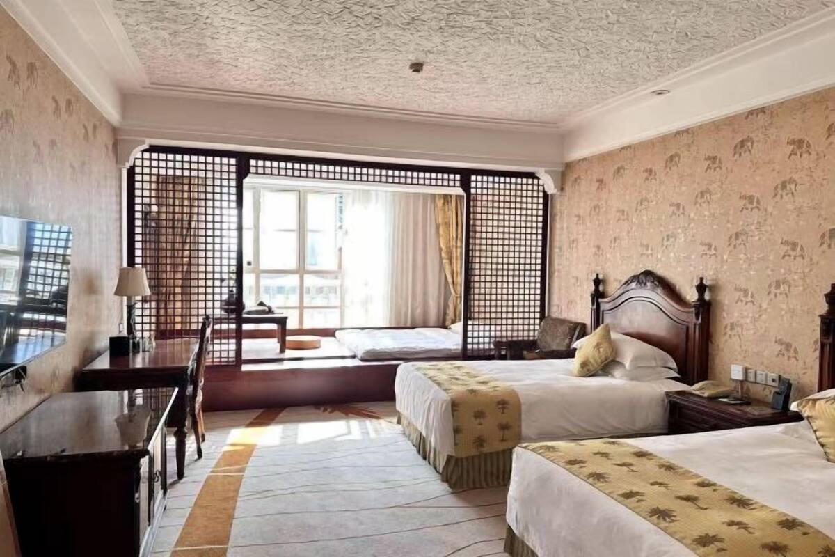 A hotel room with two beds, a desk, and a large window.