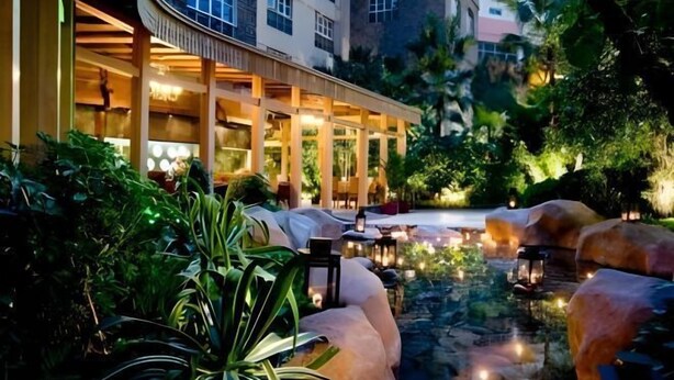 A serene outdoor seating area with a water feature, surrounded by lush greenery and a building with large windows and warm lighting. - the First World Hotel (Songcheng Hangzhou Paradise Tourist Area) (Hangzhou)