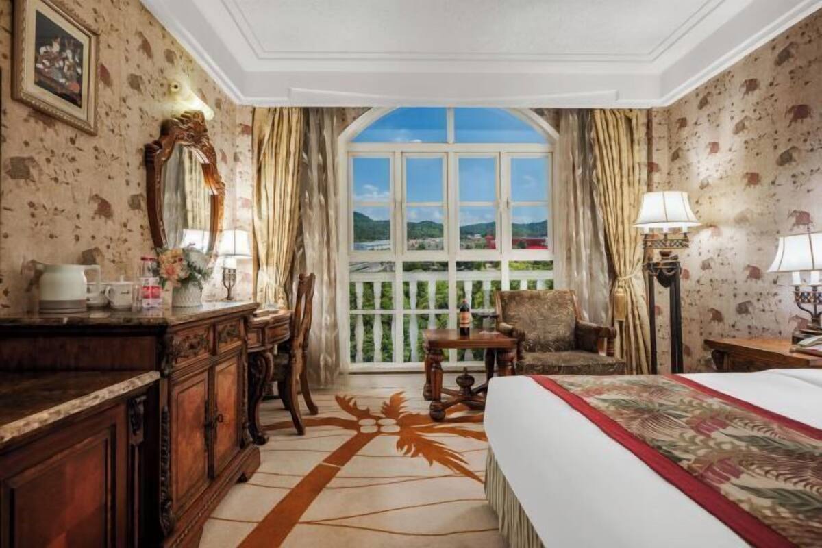 A room with a large window, a bed, a desk, a chair, and a dresser.