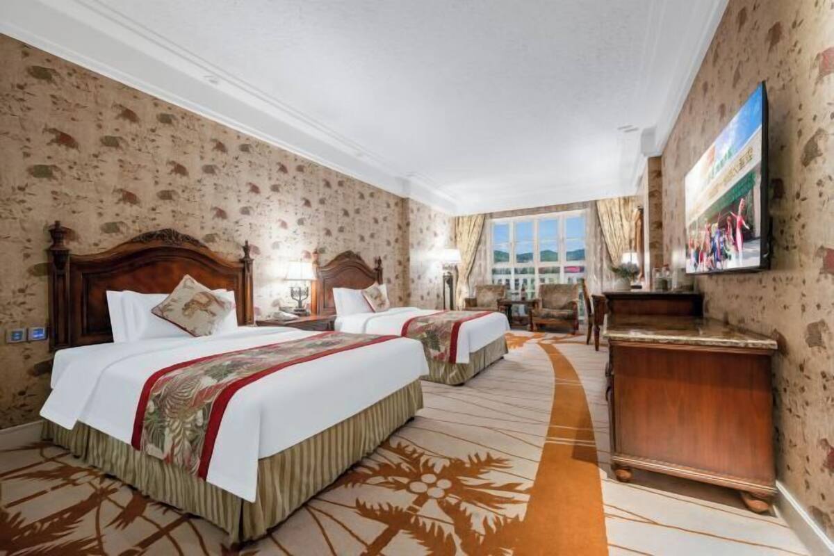 A hotel room with two beds, a wooden headboard, a TV, and a desk.