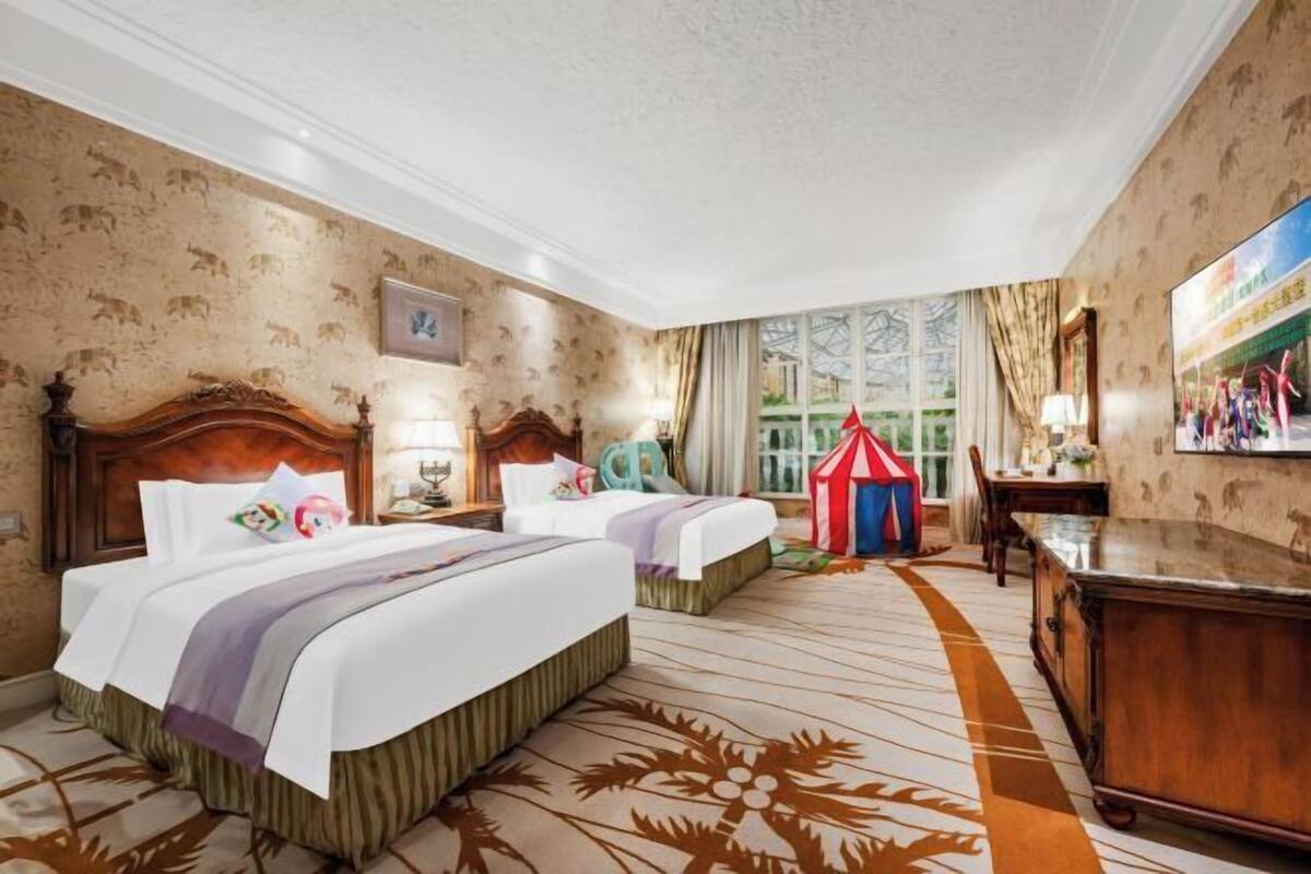 A hotel room with two beds, a large window with a view, a wooden headboard, and a small tent-like structure.