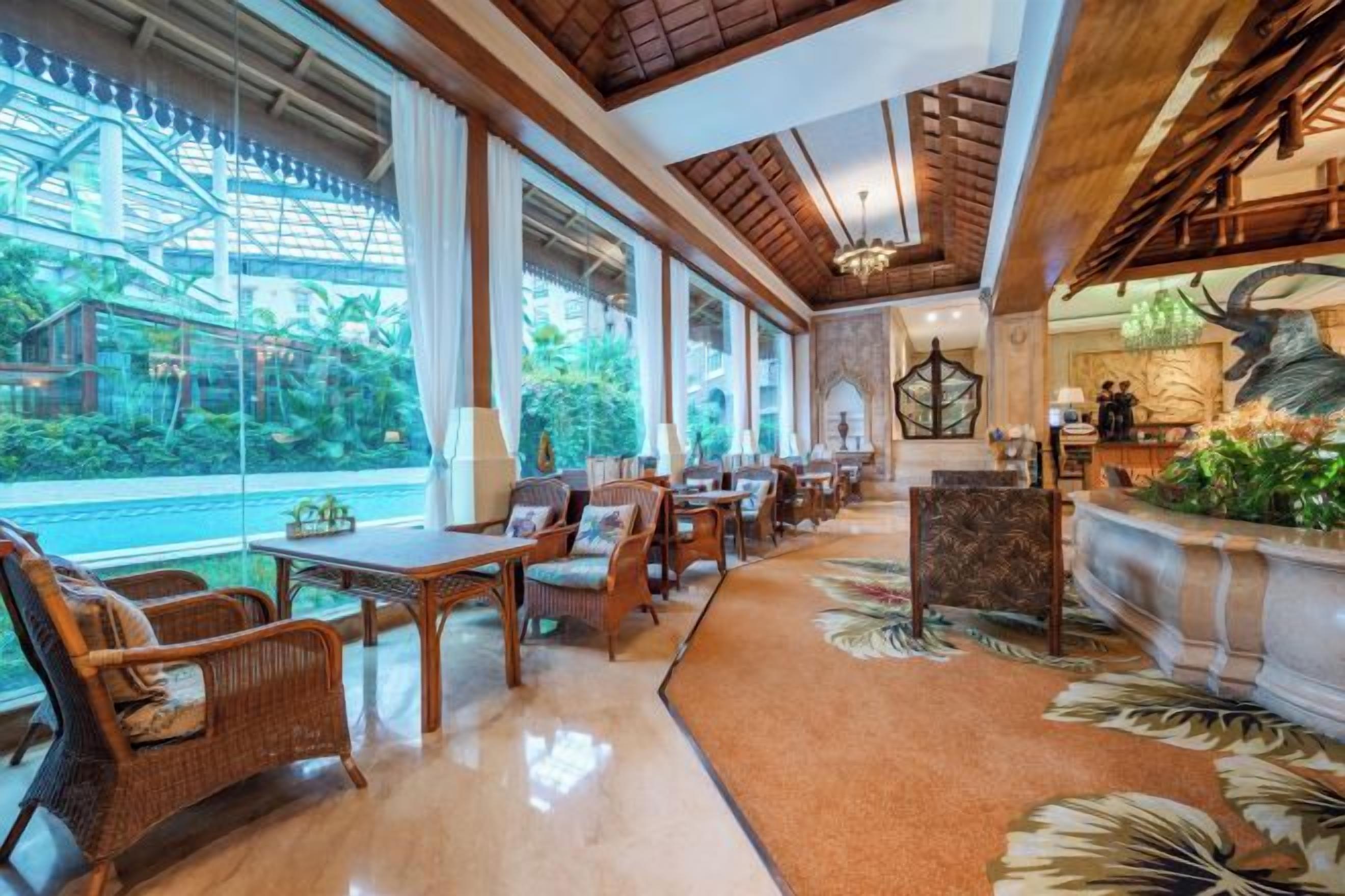 A hotel lobby with a long dining area, large windows, and a reception desk.