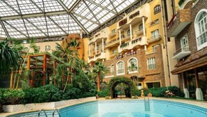 A large indoor swimming pool with a glass ceiling, surrounded by lush greenery and multi-story buildings with balconies. - the First World Hotel (Songcheng Hangzhou Paradise Tourist Area) (Hangzhou)