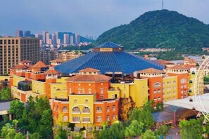 Un hotel con un edificio centrale caratteristico dal tetto blu, circondato da edifici colorati, sullo sfondo di una collina e del profilo urbano.