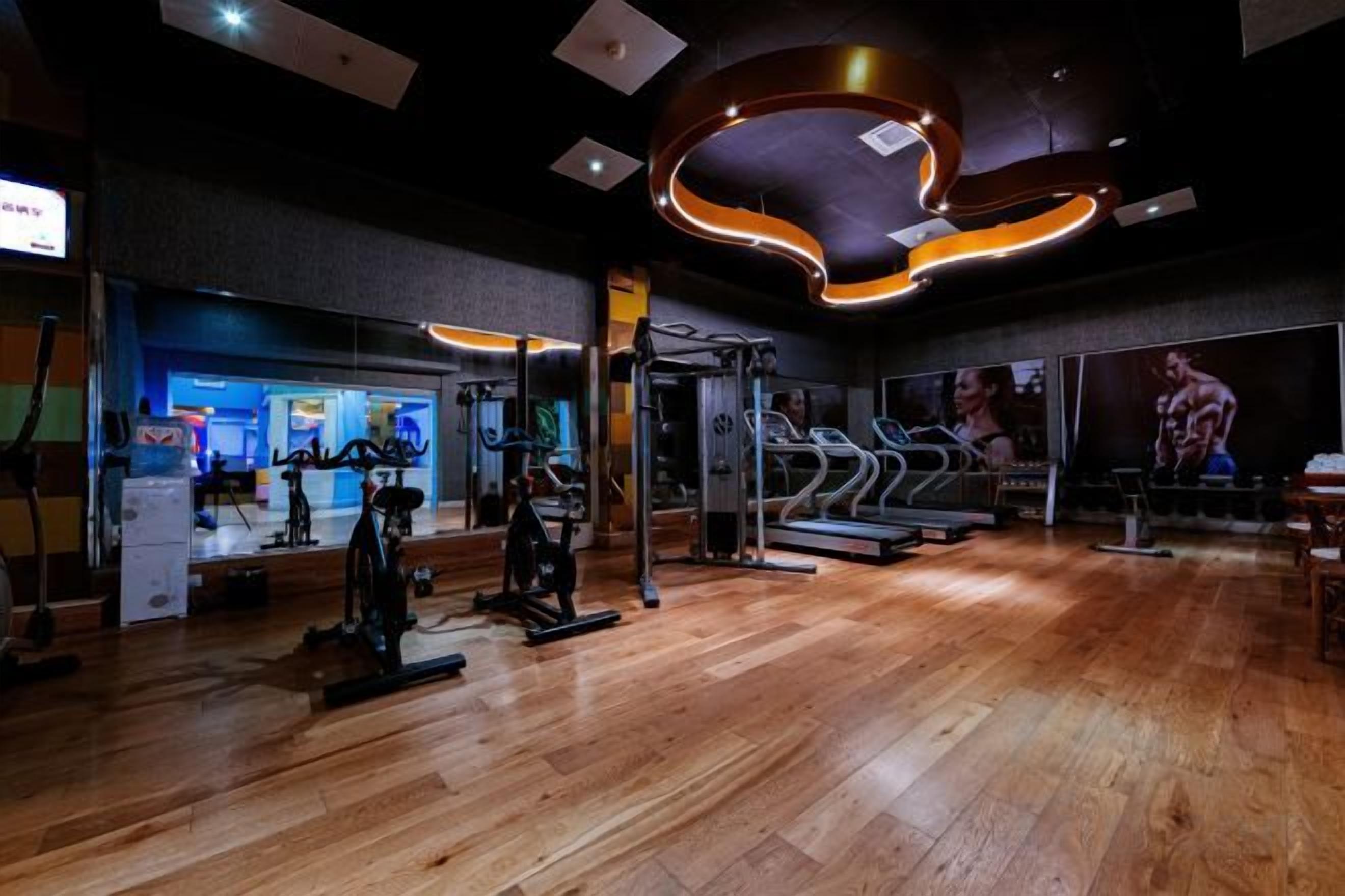 Un gimnasio con equipamiento de ejercicio, cintas de correr y suelo de madera.